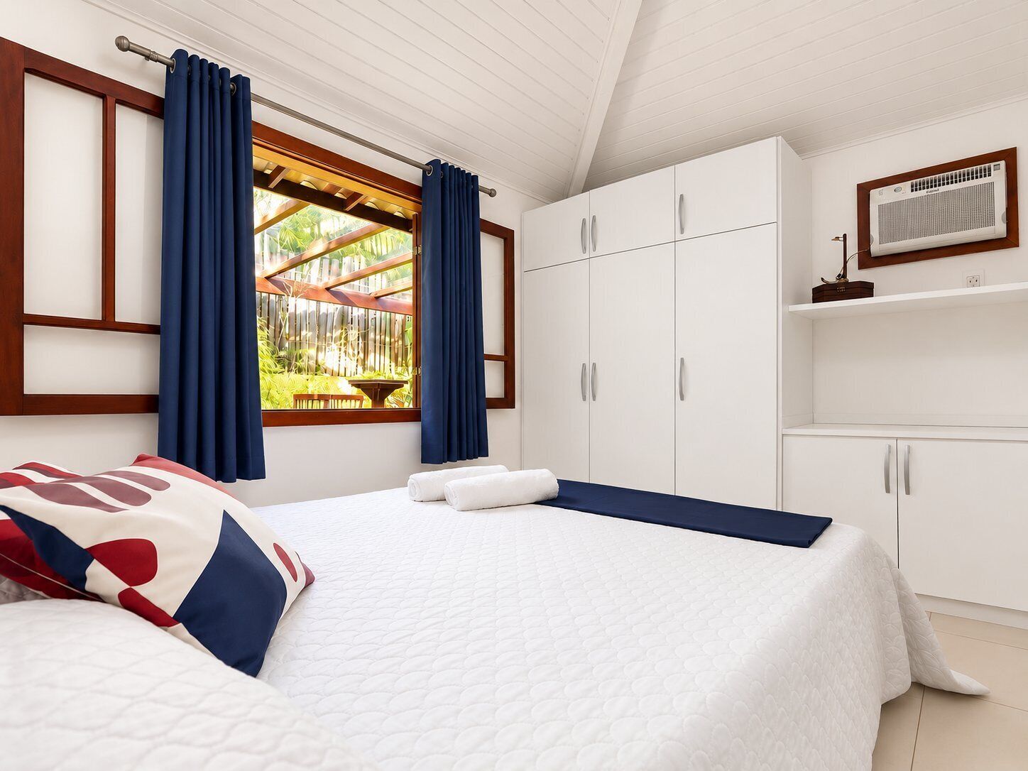Un dormitorio con cama, ventana con cortinas, armario y aire acondicionado de pared.