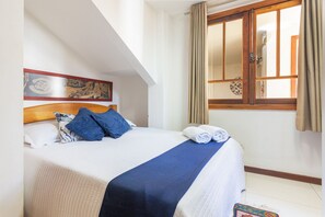 Una cama bien hecha con colcha azul y blanca, cabecera de madera y un tapiz decorativo.