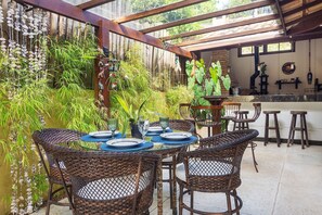 A covered outdoor dining area with wicker chairs and a glass table set for four.