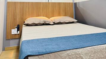 Un dormitorio moderno con una cama, un televisor montado y una mesita de noche con un control remoto.