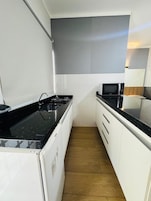 Una cocina compacta con armarios blancos, encimera negra, microondas integrado y estufa.