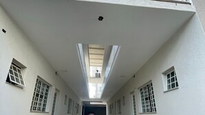 A long, narrow hallway with a high ceiling, large windows, and a car parked at the end. - Residencial Aurelio Souza (Pouso Alegre)