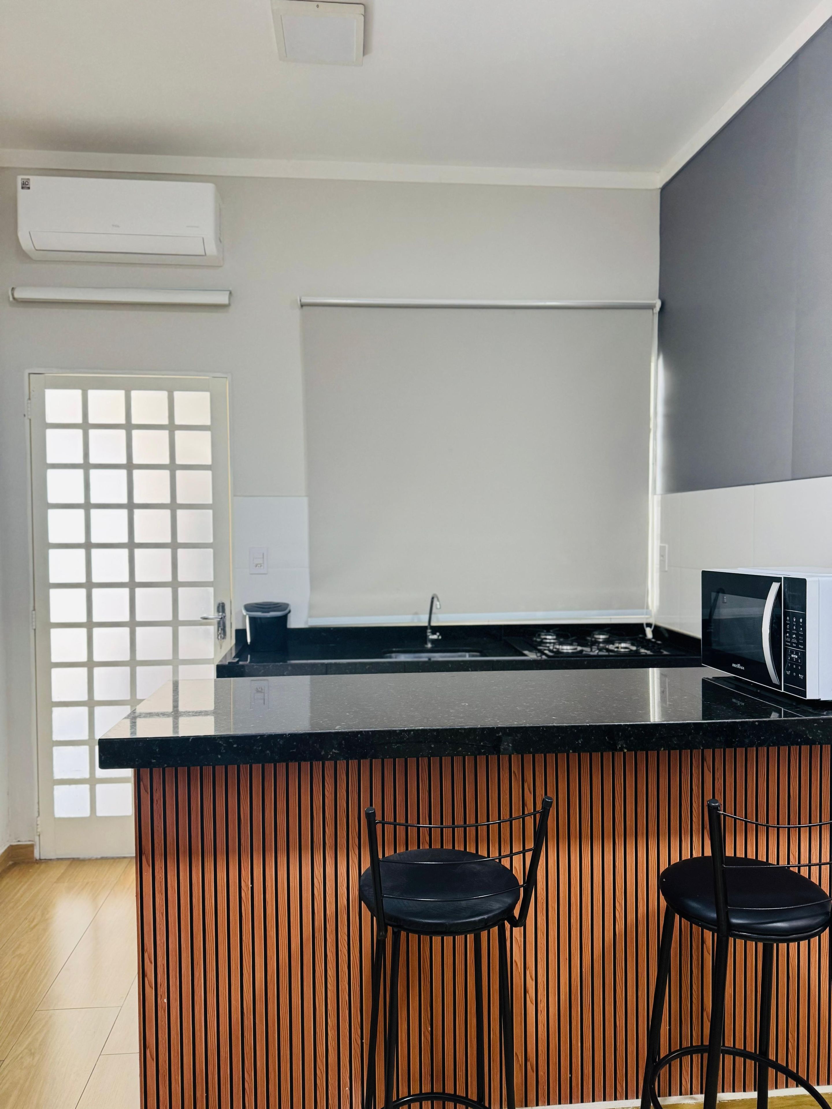 A modern kitchen with a black countertop, two bar stools, a microwave, and a window with a grid pattern.
