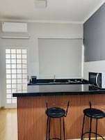 Una cocina moderna con encimera negra, dos taburetes de bar, un microondas y un ventanal con diseño de cuadrícula.