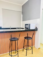 Una cocina moderna con cubierta negra, dos taburetes de bar, un microondas y un lavamanos.