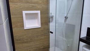 A modern bathroom with a glass shower enclosure, a white sink, and a wooden panel wall. - Residencial Aurelio Souza (Pouso Alegre)