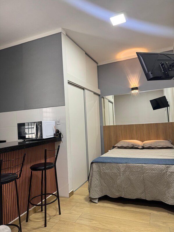 Una habitación de hotel pequeña con kitchenette, una cama con colcha estampada y un escritorio con silla.