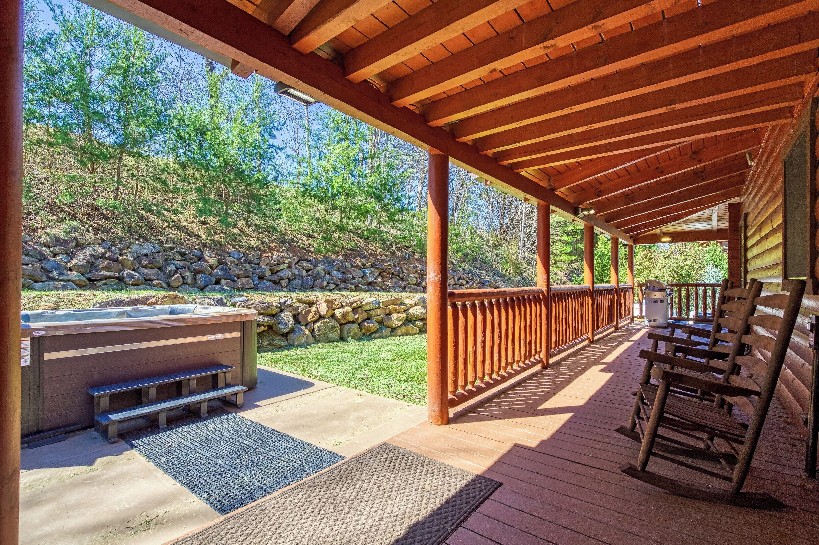 A covered deck with a hot tub, wooden benches, and a stone wall.