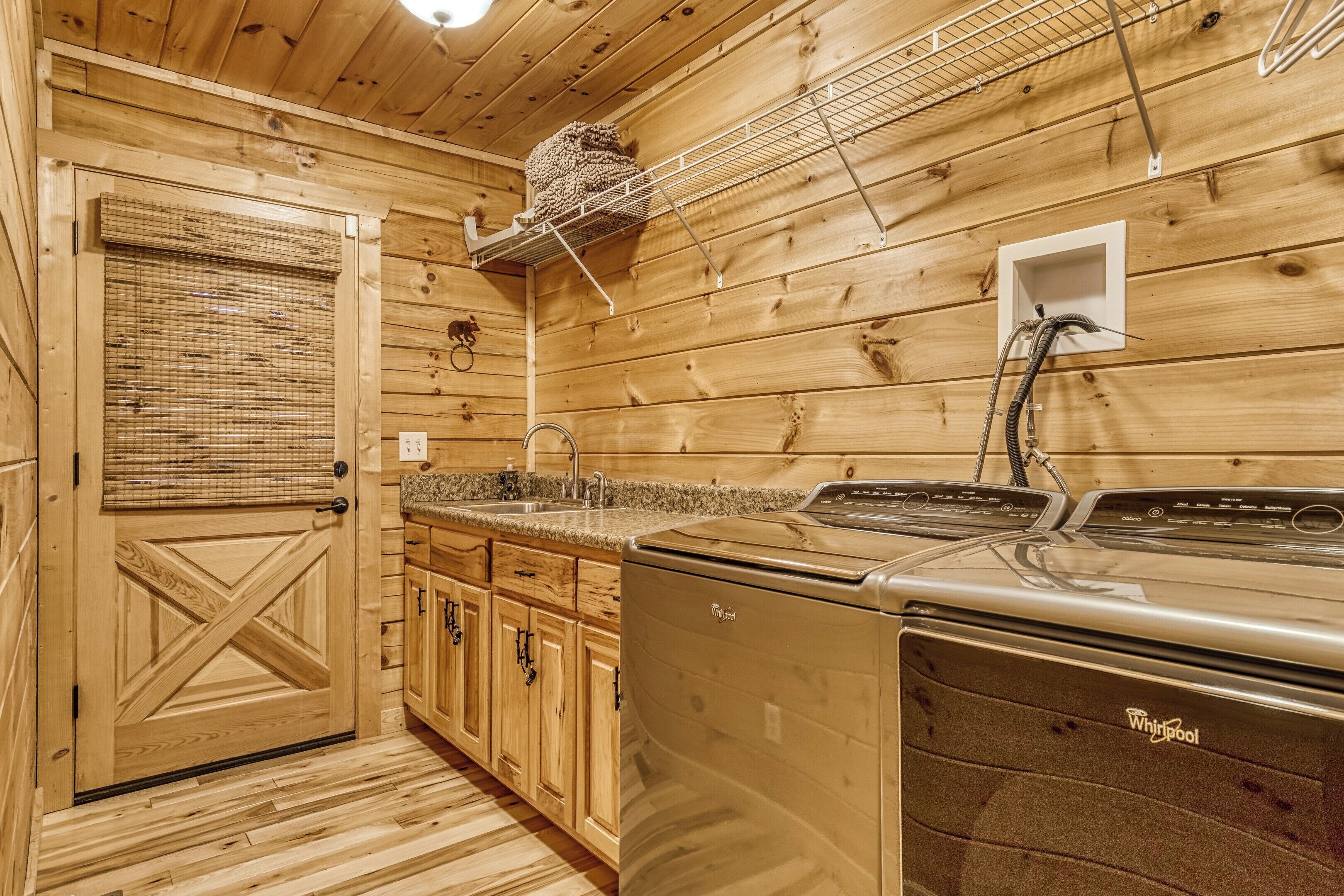 A wooden cabin interior with a Whirlpool washer and dryer, wooden cabinets, a sink, and a door with a cross design.