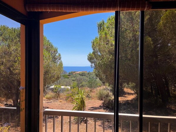 A balcony with a view of a coastal landscape, including trees and a distant view of the sea.