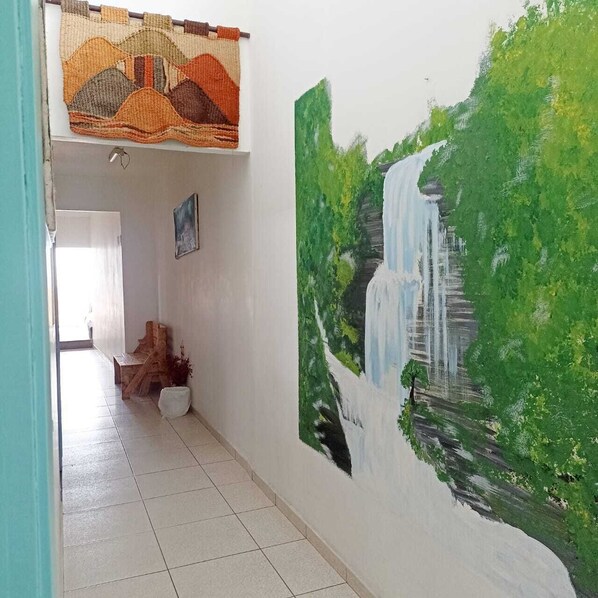A hallway with a mural of a waterfall, a woven tapestry, and a wooden sculpture.