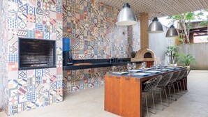 Una cocina exterior con salpicadero de azulejos, horno empotrado y una larga mesa de comedor con sillas.