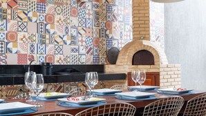 Un espacio al aire libre para comer con horno de ladrillo, sillas de metal y un revoque de azulejos.
