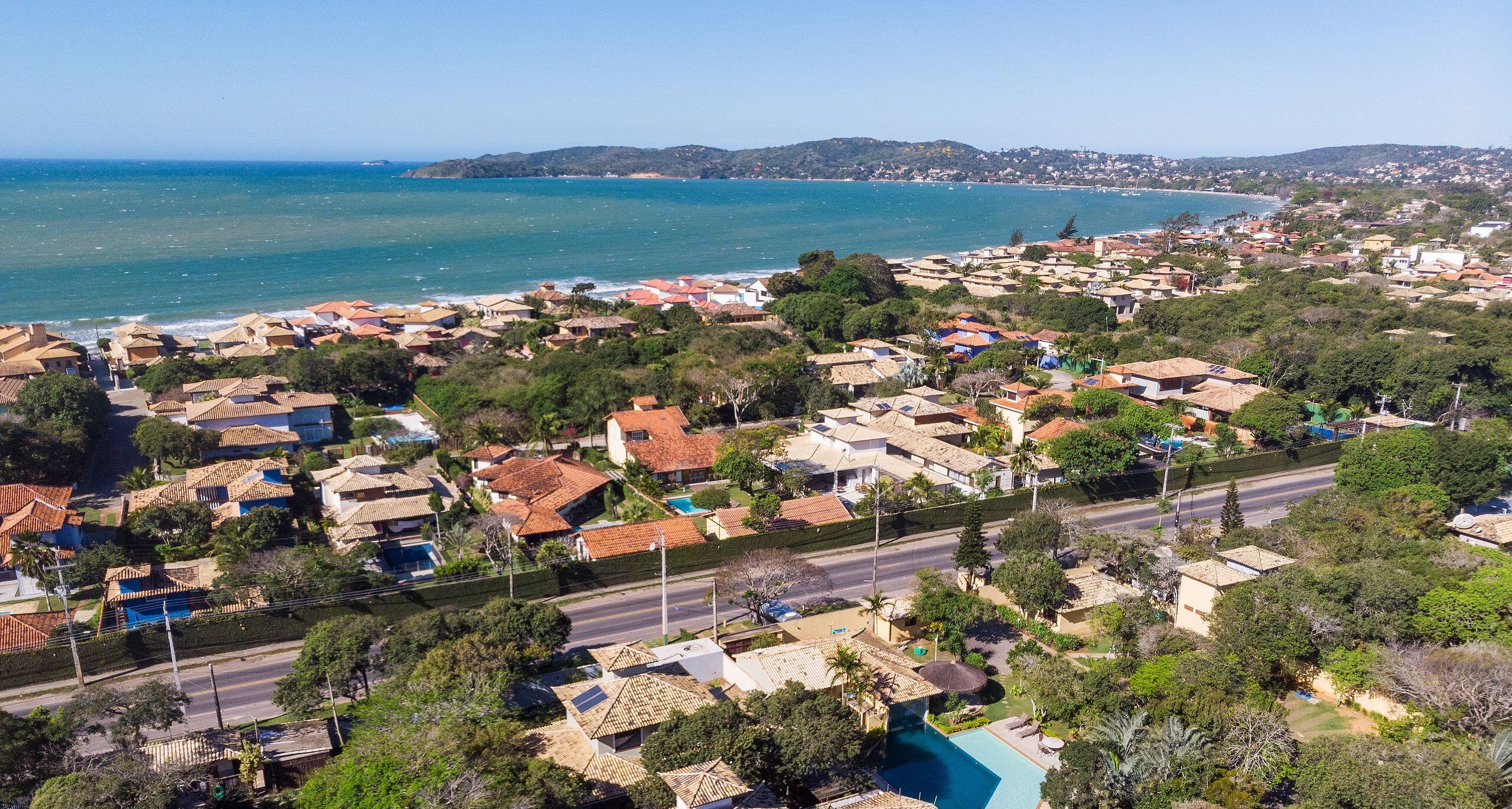 An aerial view of a coastal residential area with houses, a road, and a beach.