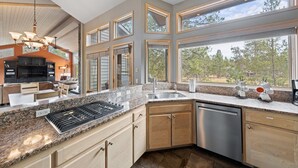 A modern kitchen with granite countertops, stainless steel appliances, and large windows offering a view of the outdoors. - TITL08 - Fantastic Sunriver Home, Hot Tub (Sunriver)
