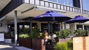 An outdoor seating area with umbrellas, a woman sitting, and a signboard listing amenities like restaurants and a supermarket.