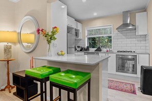 A modern kitchen with a central island, bar stools, a stove, and a window with blinds. - Seaside Bougainvillea Retreat close to Beaches (Auckland North Shore)