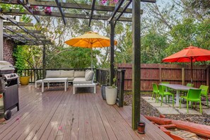 A wooden deck with outdoor furniture, including a sofa, a table, and chairs, under a pergola with hanging lights. - Seaside Bougainvillea Retreat close to Beaches (Auckland North Shore)