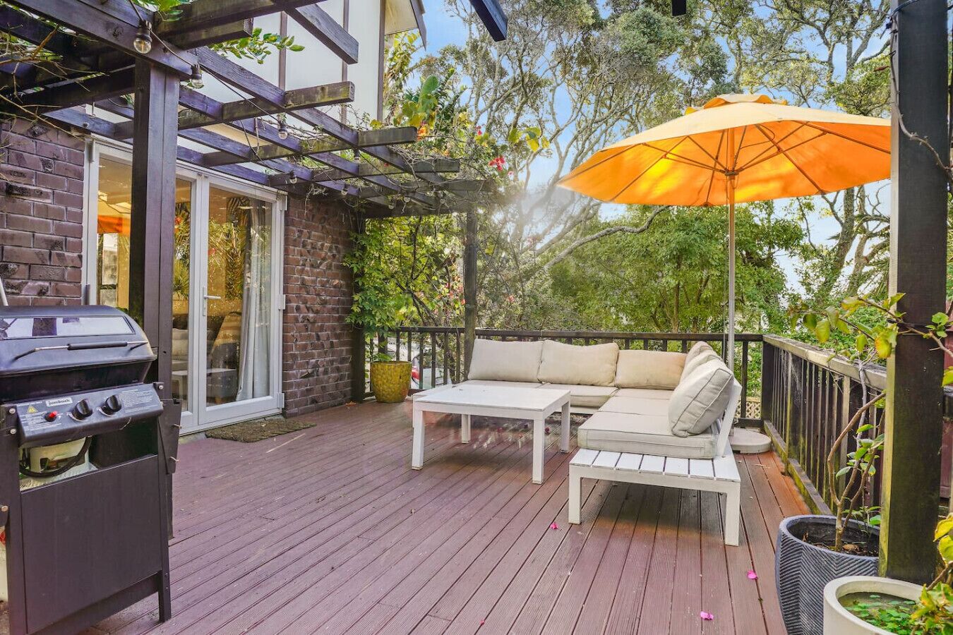 An outdoor deck with a grill, a white sofa, and an orange umbrella.