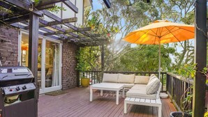 An outdoor deck with a grill, a white sofa, and an orange umbrella.