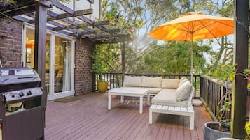An outdoor deck with a grill, a white sofa, and an orange umbrella.