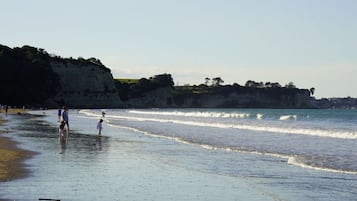 A beach with people walking along the shore, cliffs in the background, and waves approaching the beach.