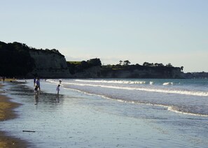 Ein Strand mit Menschen, die am Ufer entlanggehen, Klippen im Hintergrund und anstehenden Wellen.
