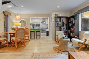 A spacious living area with a dining set, a bookshelf, and a view into the kitchen. - Seaside Bougainvillea Retreat close to Beaches (Auckland North Shore)
