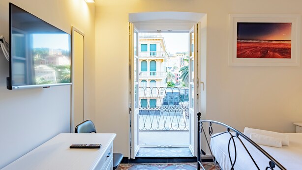A hotel room with a bed, a desk, a TV, and a balcony with a view of buildings.