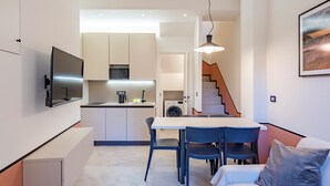 A modern kitchen with a dining area, a sofa, and a staircase leading to an upper level.