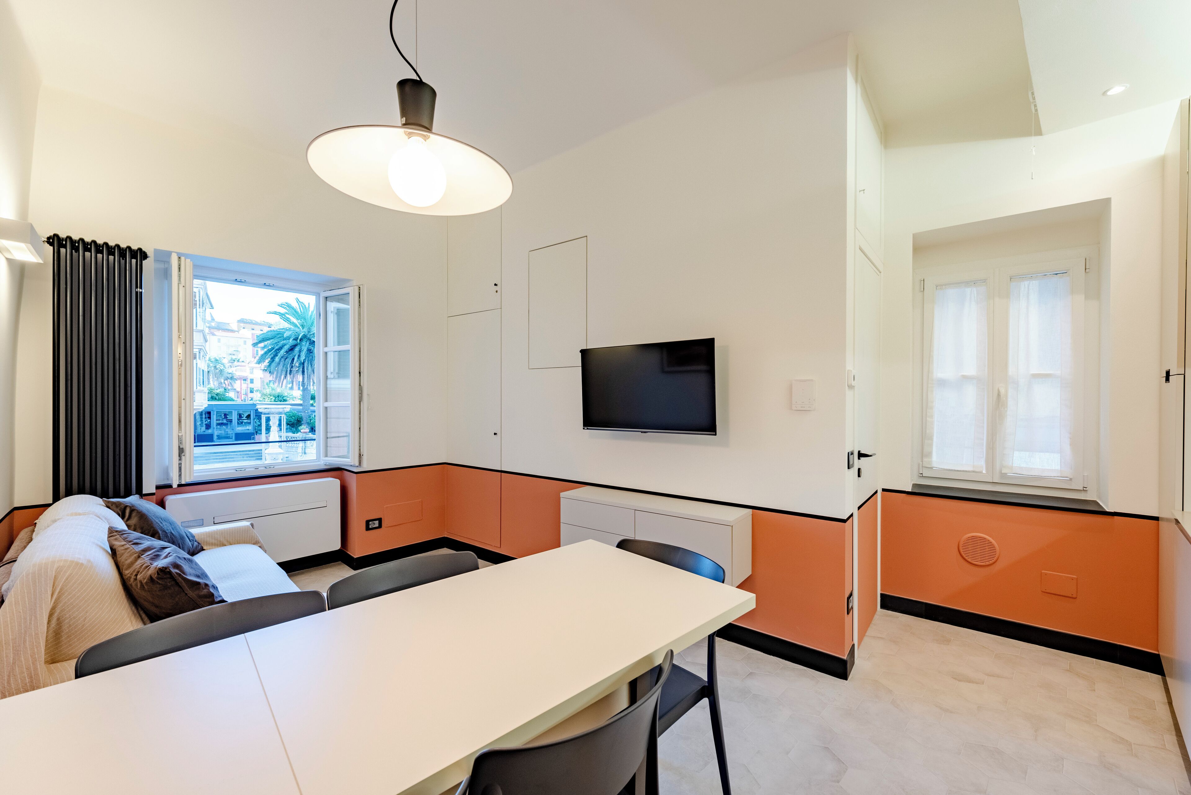 Ein modernes Zimmer mit Esstisch, Stühlen, einem an der Wand befestigten Fernseher und einem Fenster mit Vorhängen.