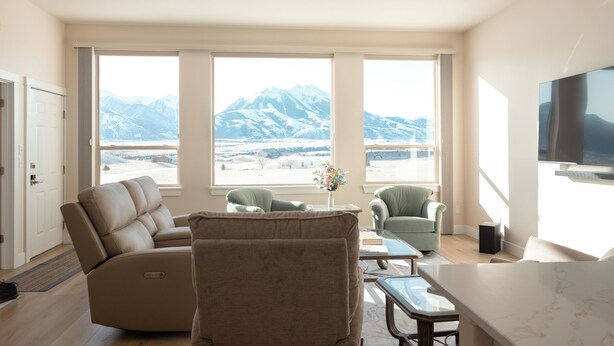 Un salon moderne comprenant un canapé, des fauteuils, une table basse et un téléviseur. De grandes fenêtres offrent une vue sur les montagnes.