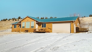 Une cabane en bois à deux étages, dotée d’un garage, située dans un paysage enneigé sous un ciel dégagé.