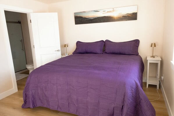 A bedroom with a large bed, a painting on the wall, and a door leading to a bathroom.