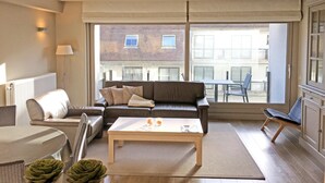 A modern living room with a sofa, coffee table, and a view of the outside balcony. - Apartment in Knokke Near Beach and Casino (Knokke-Heist)