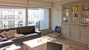 A living room with a sofa, coffee table, and a cabinet with glass doors. - Apartment in Knokke Near Beach and Casino (Knokke-Heist)