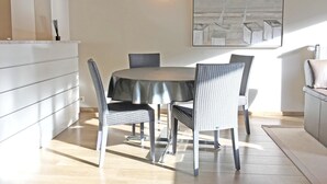 A dining area with a round table, four chairs, a white cabinet, and a painting on the wall. - Apartment in Knokke Near Beach and Casino (Knokke-Heist)