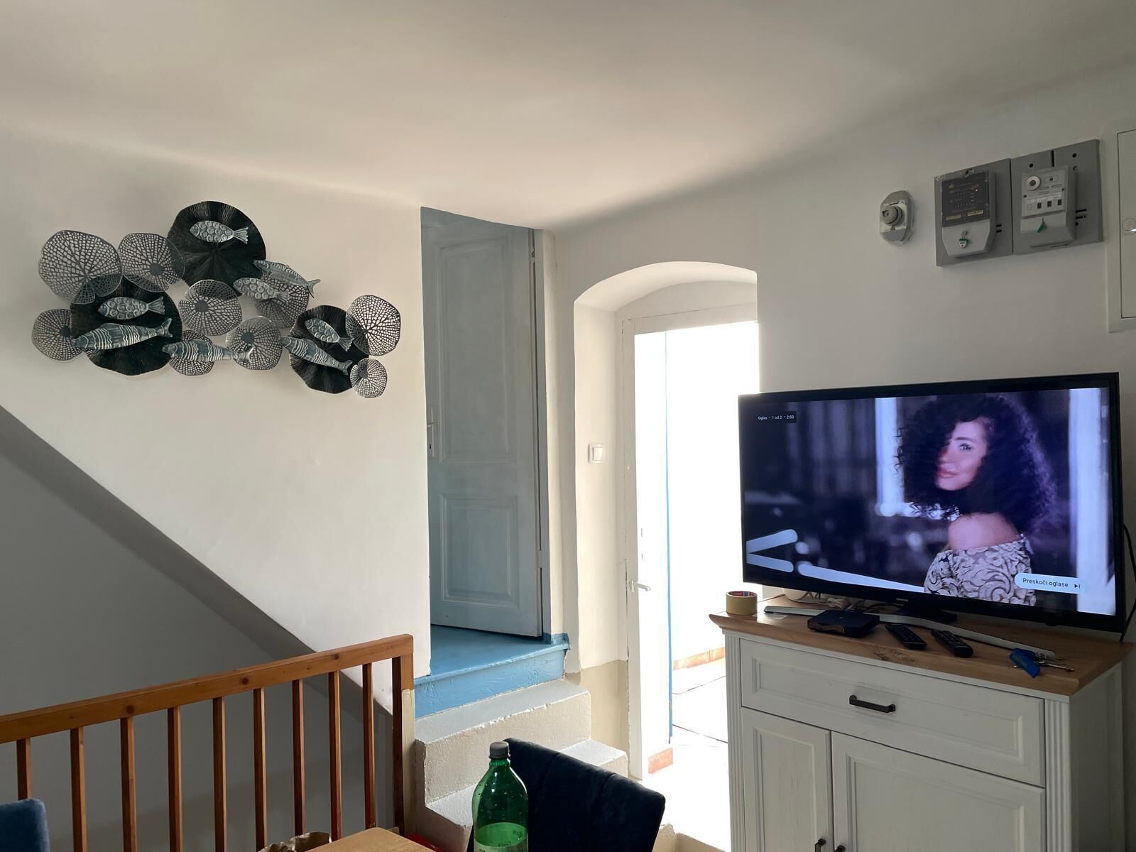 Ein Wohnzimmer mit Fernseher, Wanddekoration, einer Treppe und einem weißen Schrank.