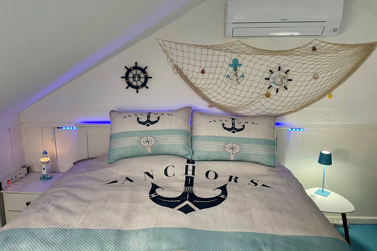 Un dormitorio con una cama con ropa de cama de temática náutica, un ventilador de techo y un equipo de aire acondicionado.