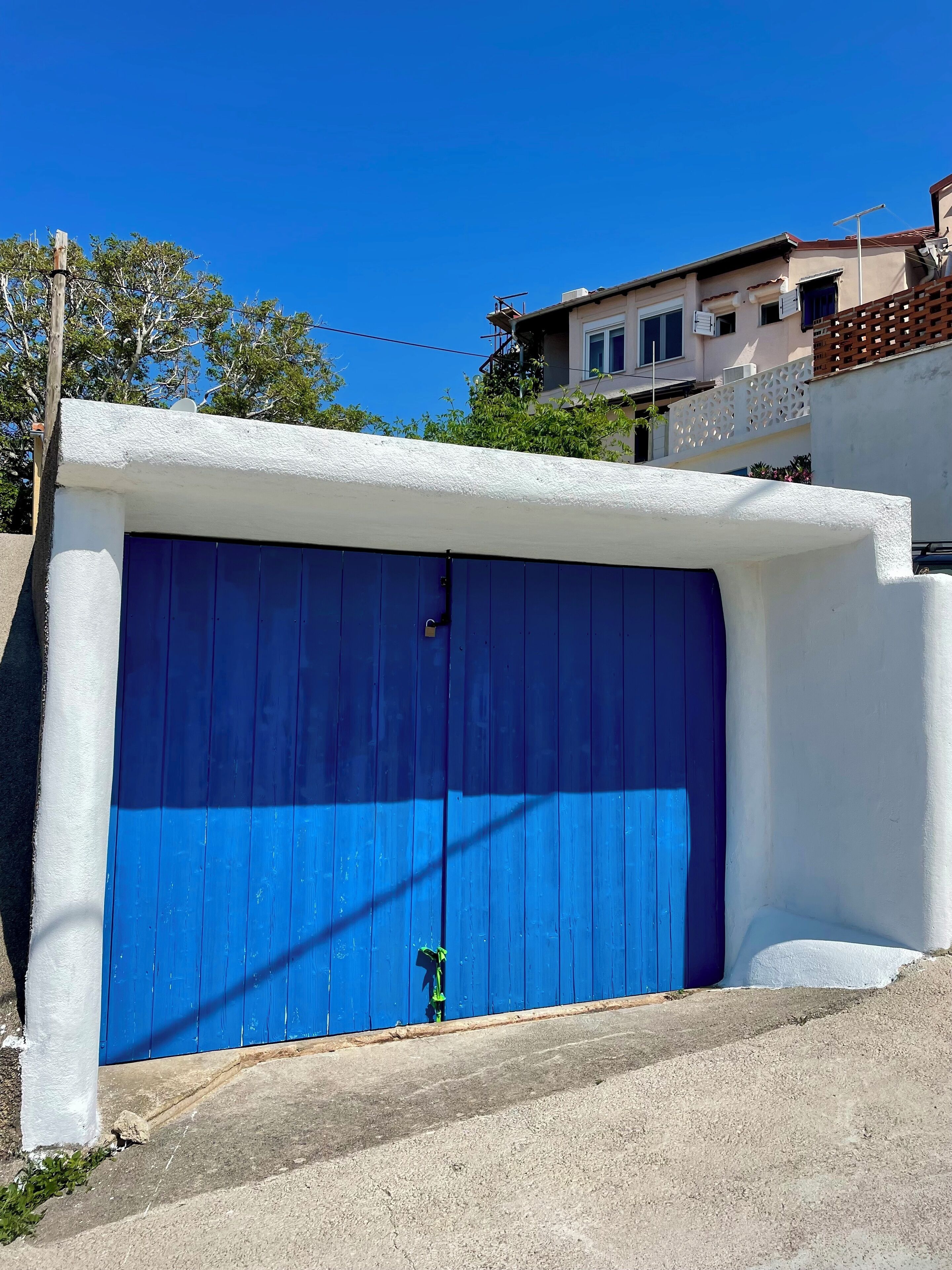 Eine blaue Garagentür neben einer weißen Wand und einer Betonauffahrt.