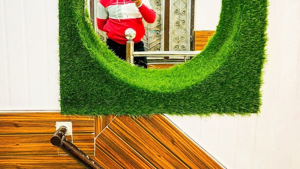 Un espejo con marco de césped artificial, una escalera de madera y una barandilla de metal.