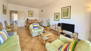 Una sala de estar con un sofá, sillones, una mesa de centro, un televisor y un comedor con una mesa y sillas.
