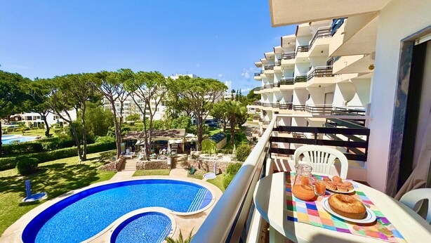 Un balcón con una mesa dispuesta para el desayuno, con vistas a una piscina y a la zona de un complejo turístico.