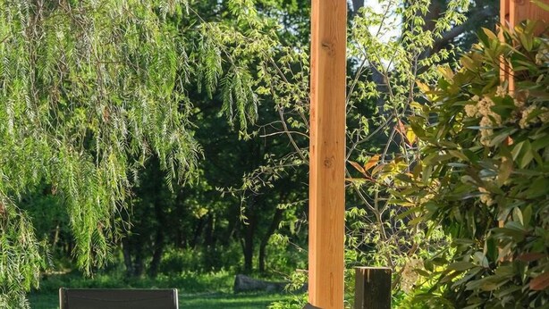 Eine Holnpergola mit Tisch und Stühlen darunter, umgeben von üppiger Vegetation und Bäumen.