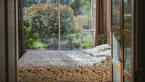 Ein Schlafzimmer mit Bett, Deckenventilator und Blick auf einen Garten durch ein großes Fenster.