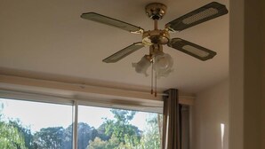 Ein Schlafzimmer mit zwei Betten, einem Deckenventilator und einem großen Fenster mit Blick auf einen Garten.