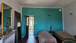 A room with teal walls, a bed, a bedside table, a mirror, and a door leading to another room. - Master bedroom with living room (Rapale)