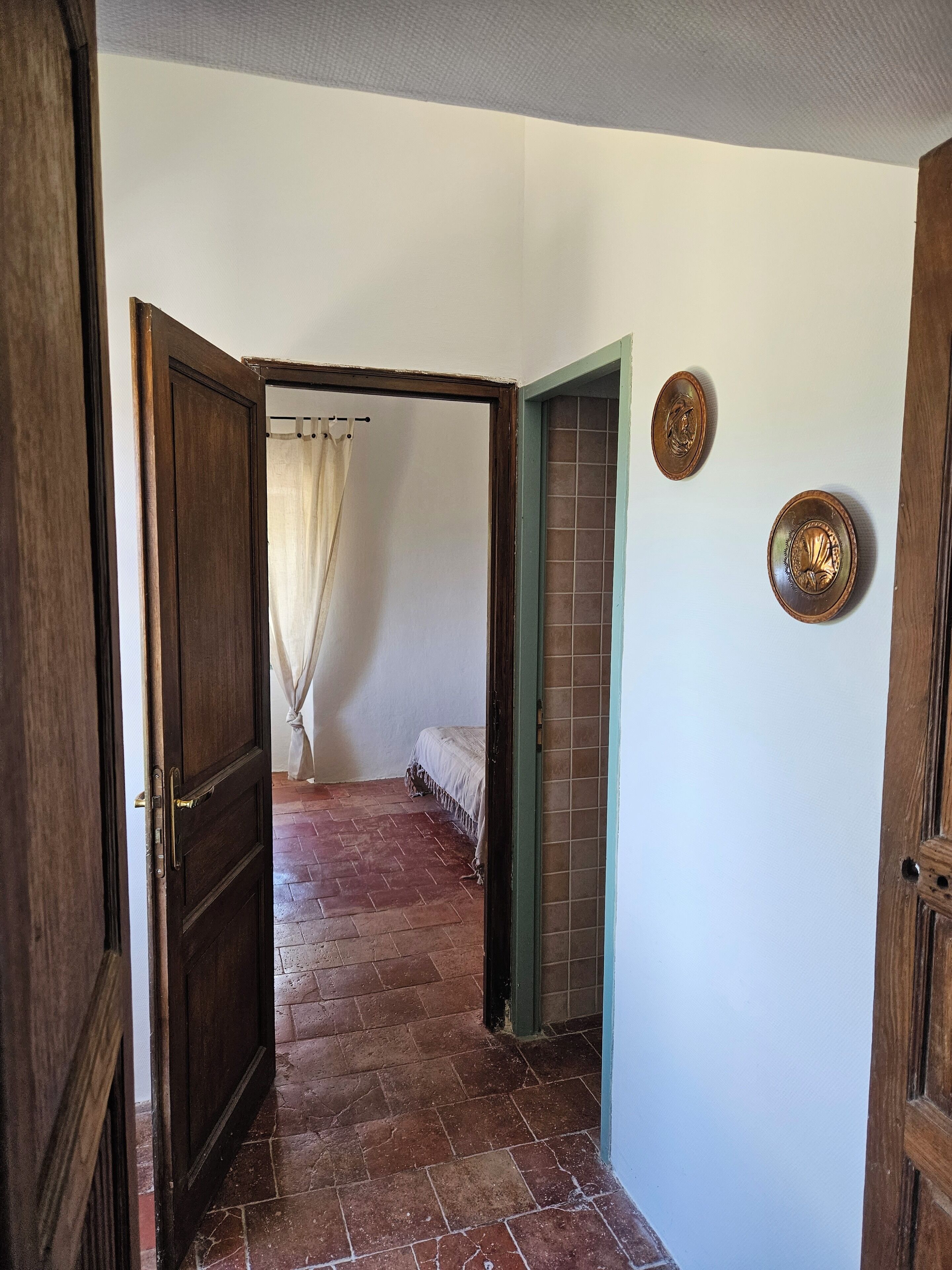 A hallway with a wooden door, a tiled wall, and a bed with a white bedspread.