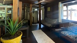 A spacious living area with a wooden ceiling, a large potted plant, and a stone fireplace. - Linda casa na Praia de Cambury - SP - 4  (Sao Sebastiao)