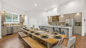 Una cocina moderna con una larga mesa de comedor, electrodomésticos integrados y un amplio ventanal.